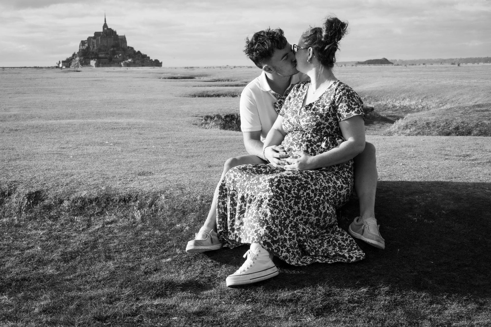 Couple s'embrassant assis dans l'herbe, le Mont-Saint-Michel au loin